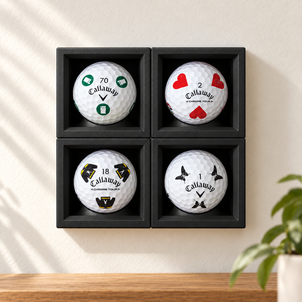 Four black single ball display cases on a wall, each holding a logo golf ball