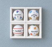 Four white single ball display cases on a wall, each holding a logo golf ball