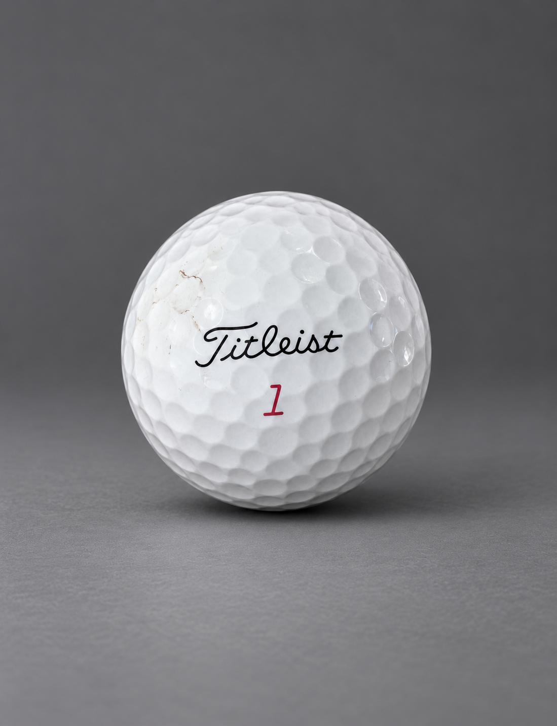 Used Titleist golf ball with light scuff marks on a graphite surface