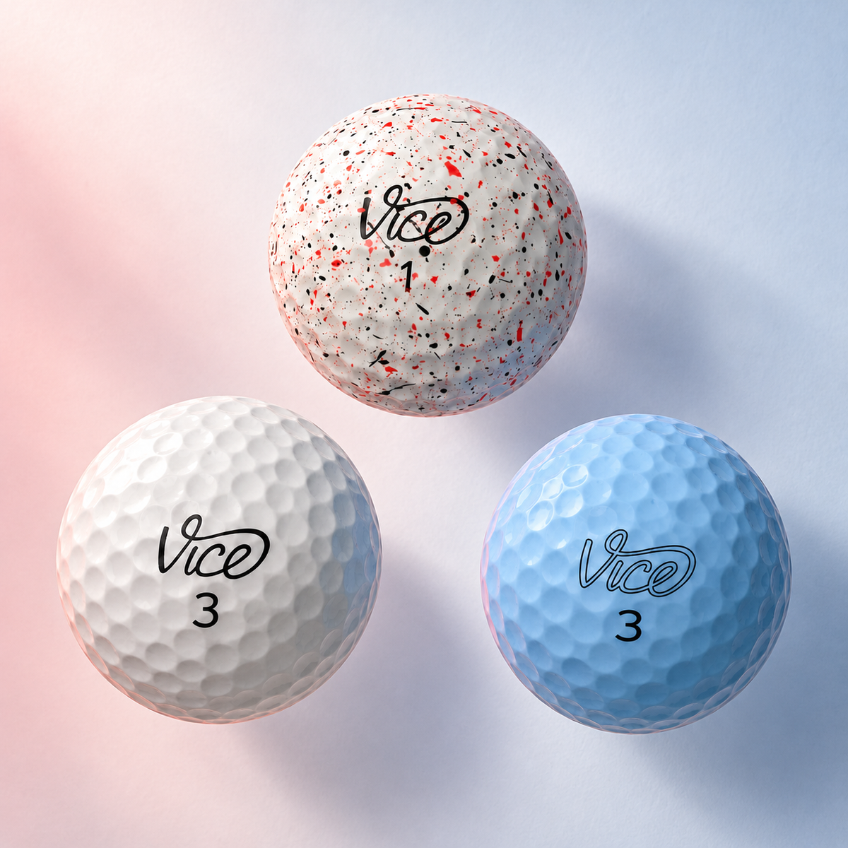 Three Vice golf balls, white, ice blue and red splatter, against a soft pink and blue background